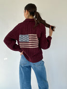 Person wearing a maroon sweater with an American flag design on the back on a white background