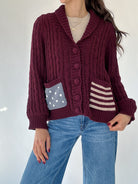 Person wearing a burgundy button front cardigan with striped and dotted patterned pockets on a white background