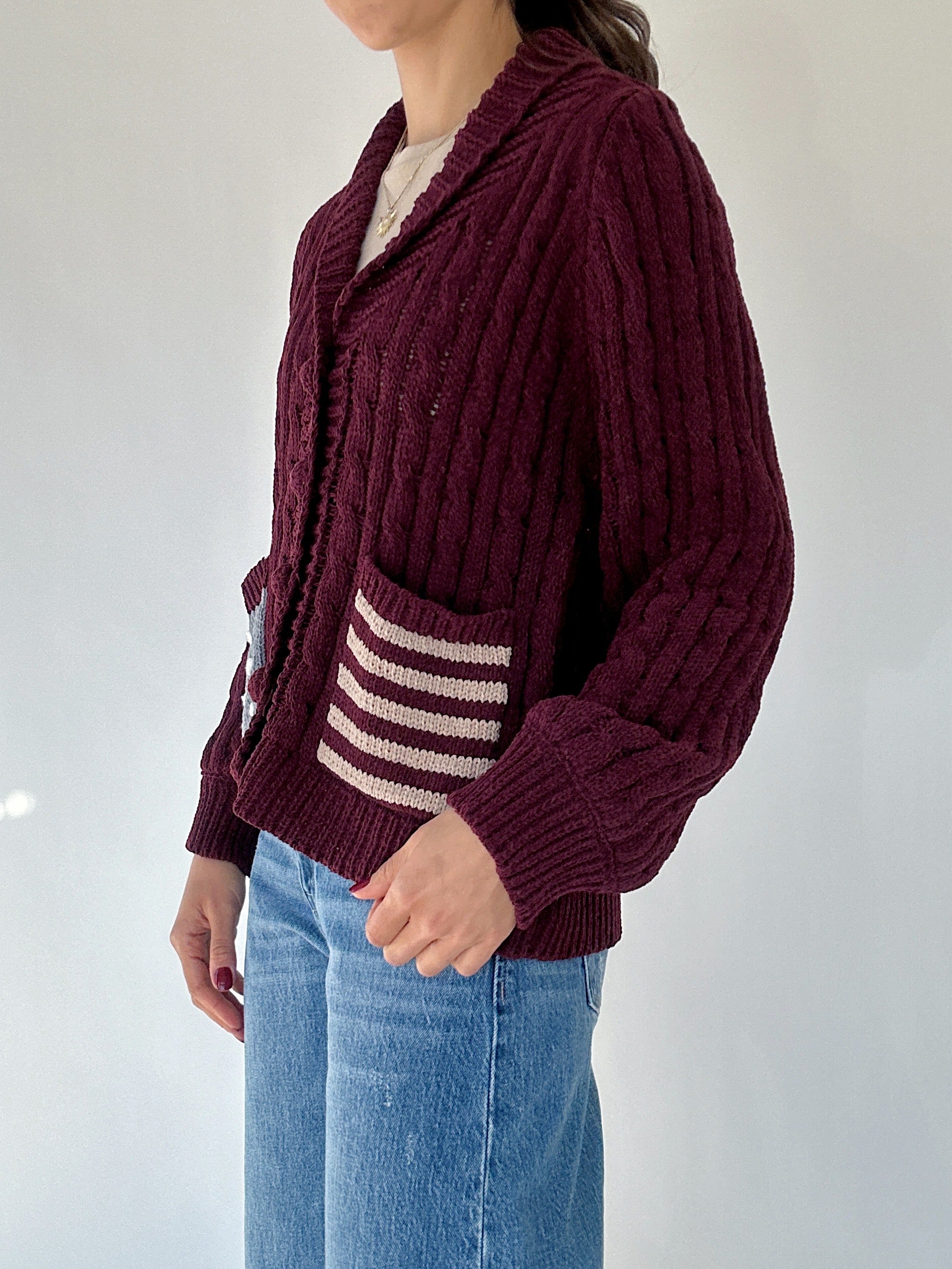 Person wearing a burgundy cardigan with a striped pocket on a white background