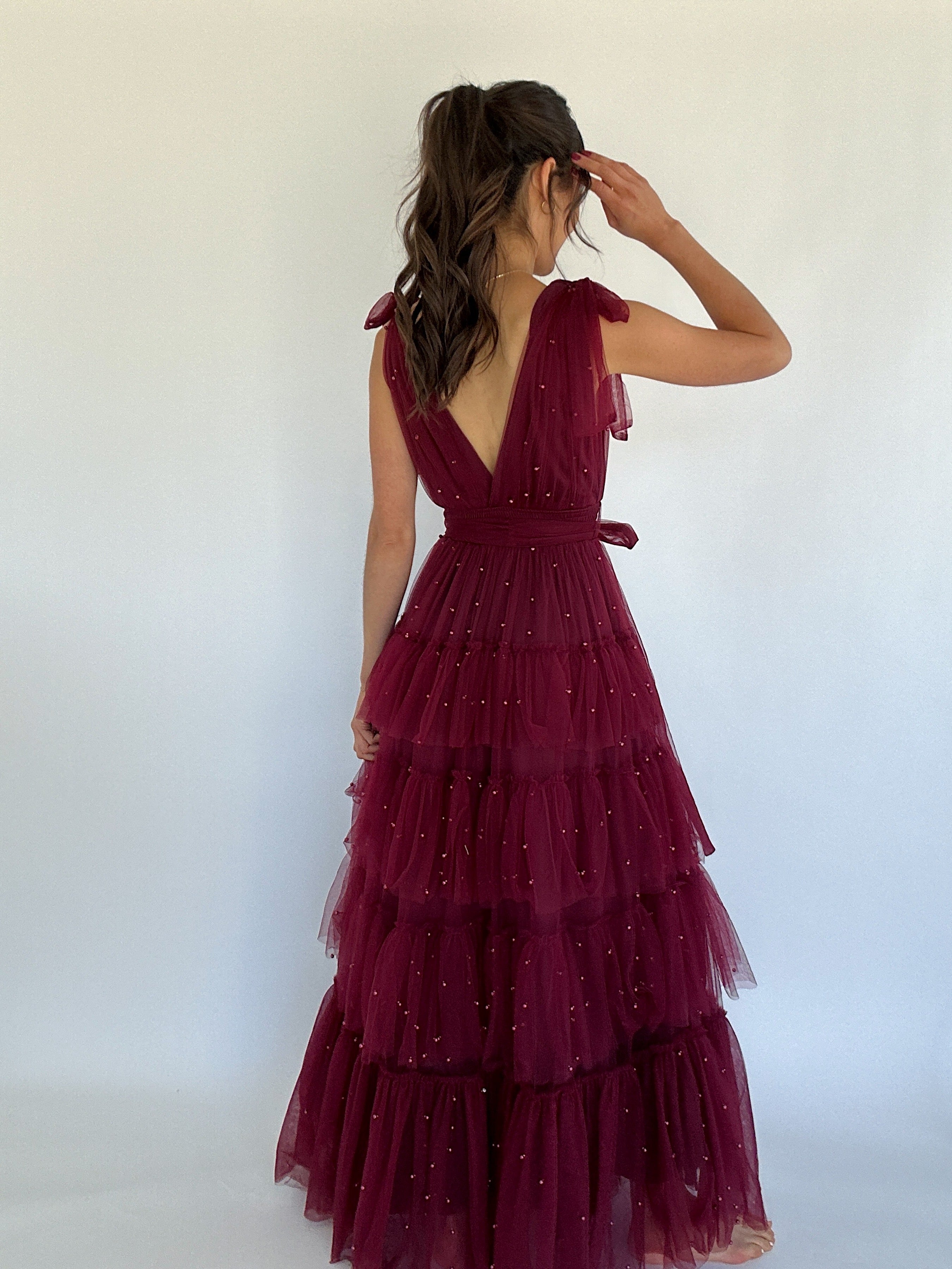 Woman wearing a burgundy, tiered dress against a white background showing back deep v