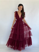 Woman wearing a burgundy evening gown with tiered tulle overlay on a white background