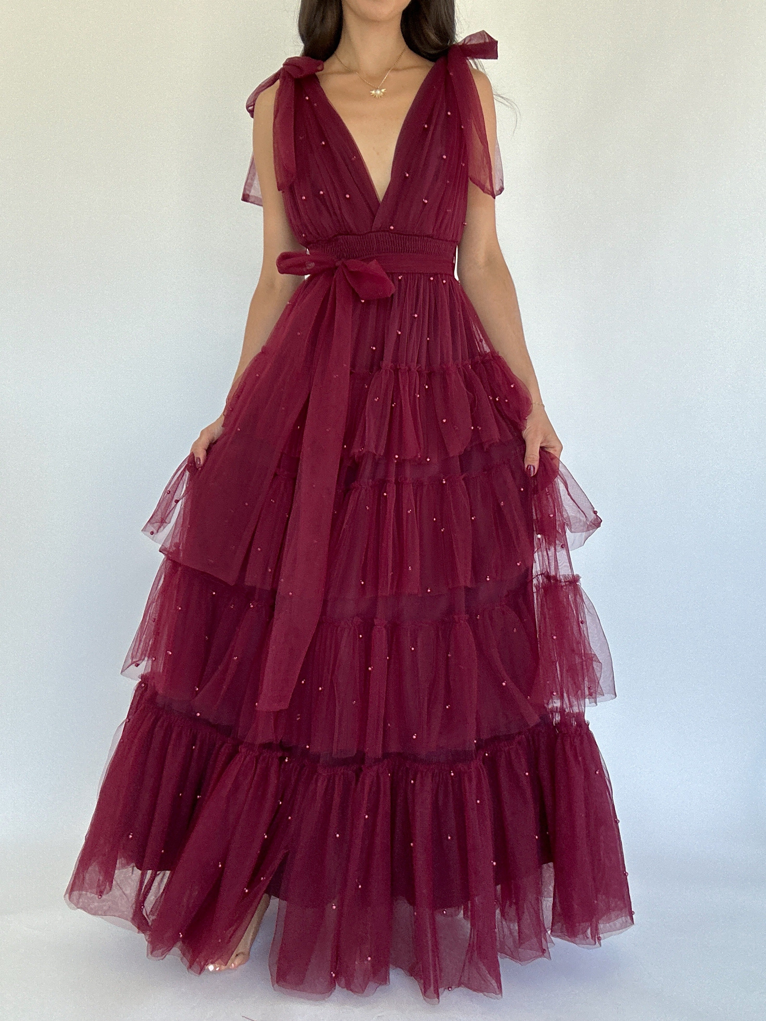 Maroon evening gown with sheer overlay and pearl embellishments on a white background