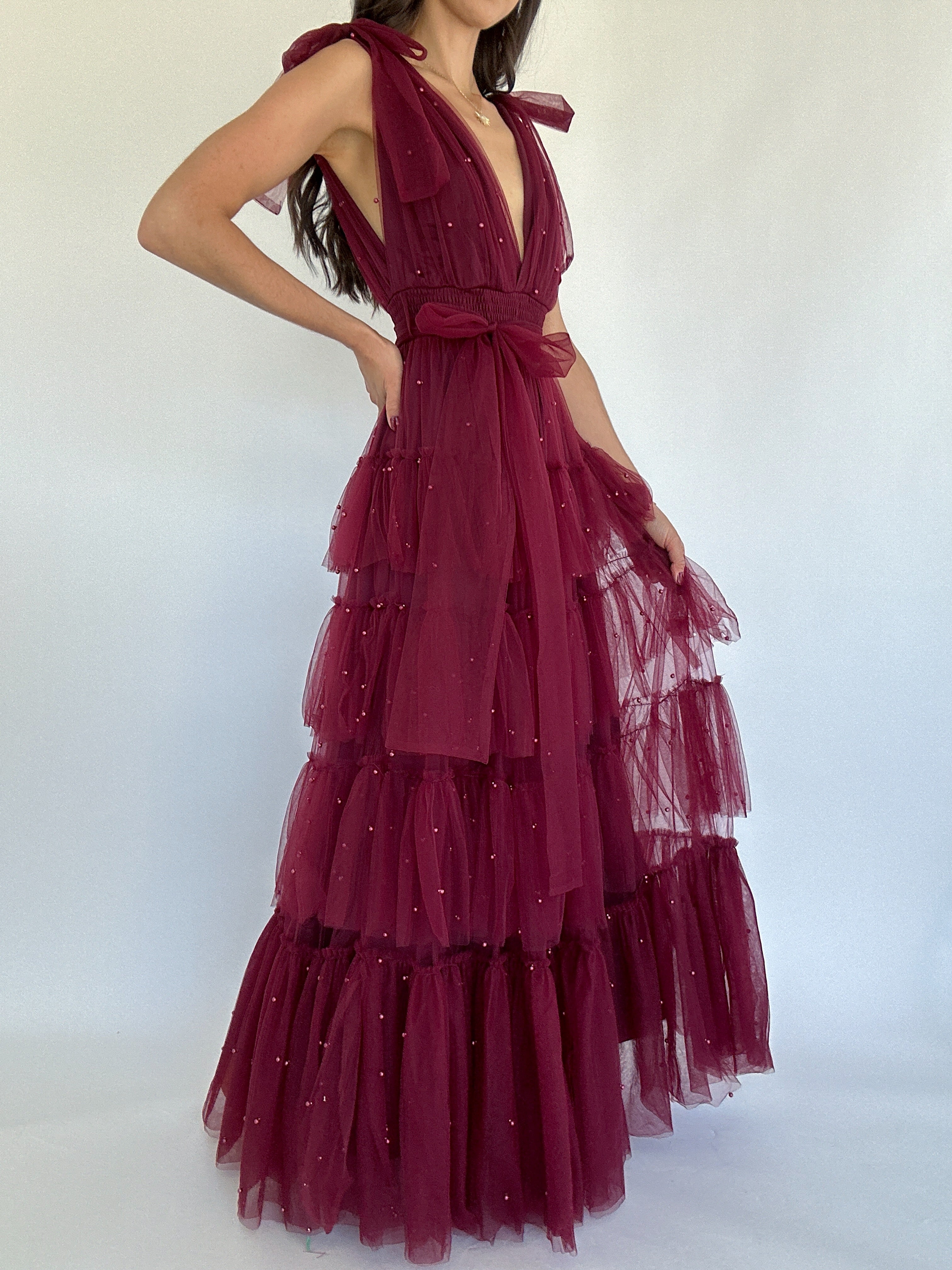 Maroon evening gown with ruffled layers on a white background showing side view
