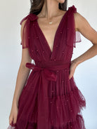 Maroon dress with pearl embellishments on a plain background to show deep v neckline and sash waist and tie straps