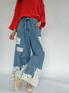 Person wearing a bright coral sweater and blue patchwork wide leg jeans on a plain background