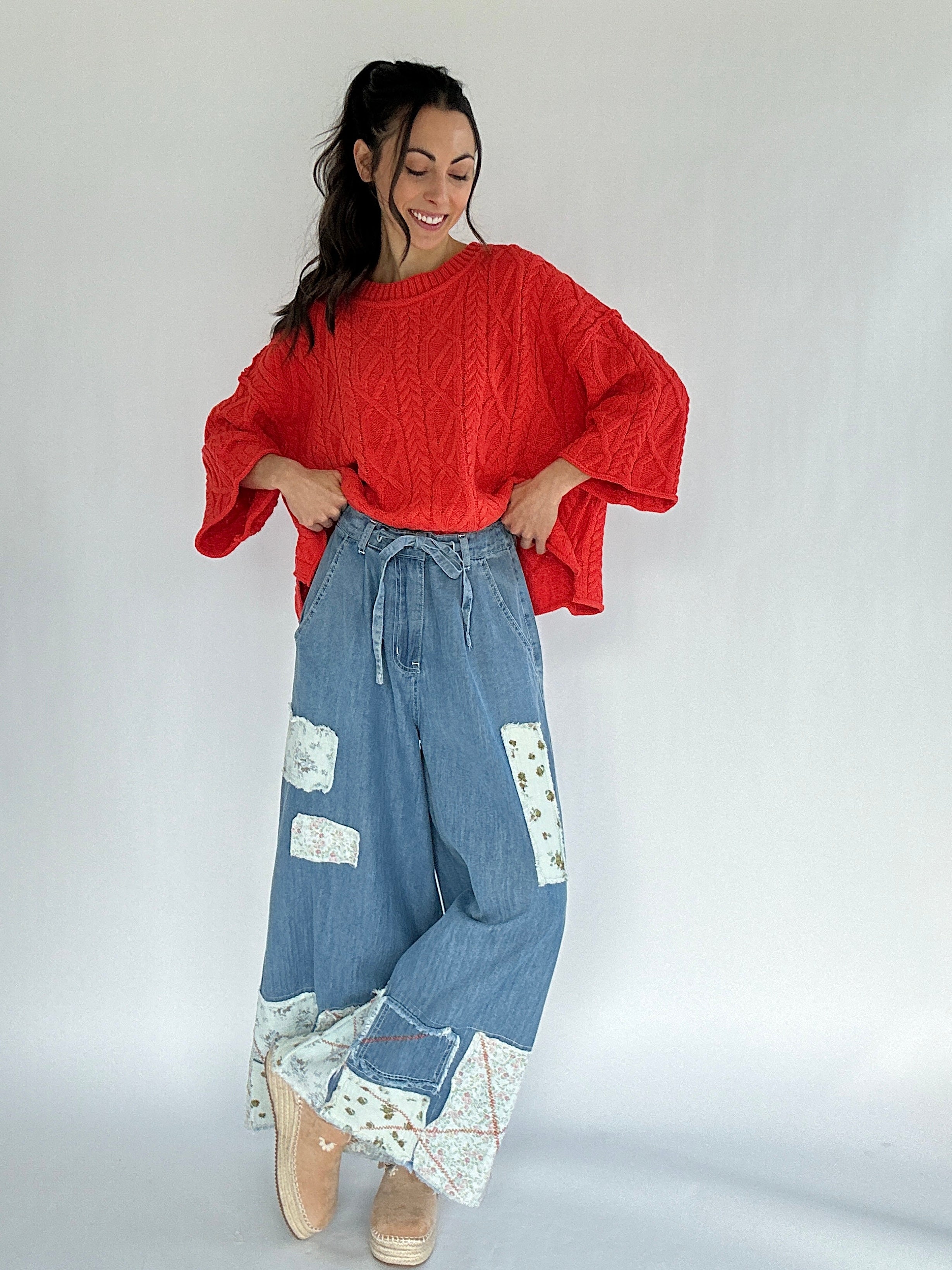 Woman wearing a bright coral sweater and blue patchwork pants on a white background