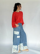 Woman wearing a bright coral sweater and blue patchwork pants on a white background