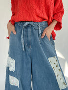 Person wearing a coral sweater and blue jeans with floral patches on a white background to show drawstring waist and side pockets