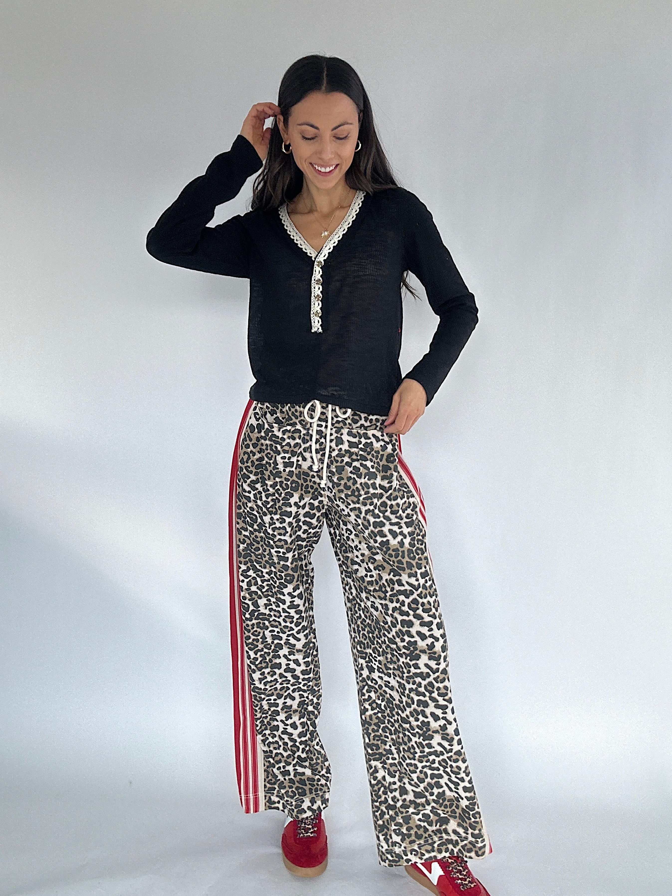 Woman wearing a black long-sleeve top and leopard print pants with red stripes on a white background