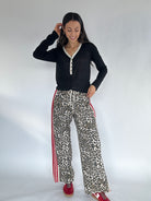 Woman wearing a black long-sleeve top and leopard print pants with red stripes on a white background