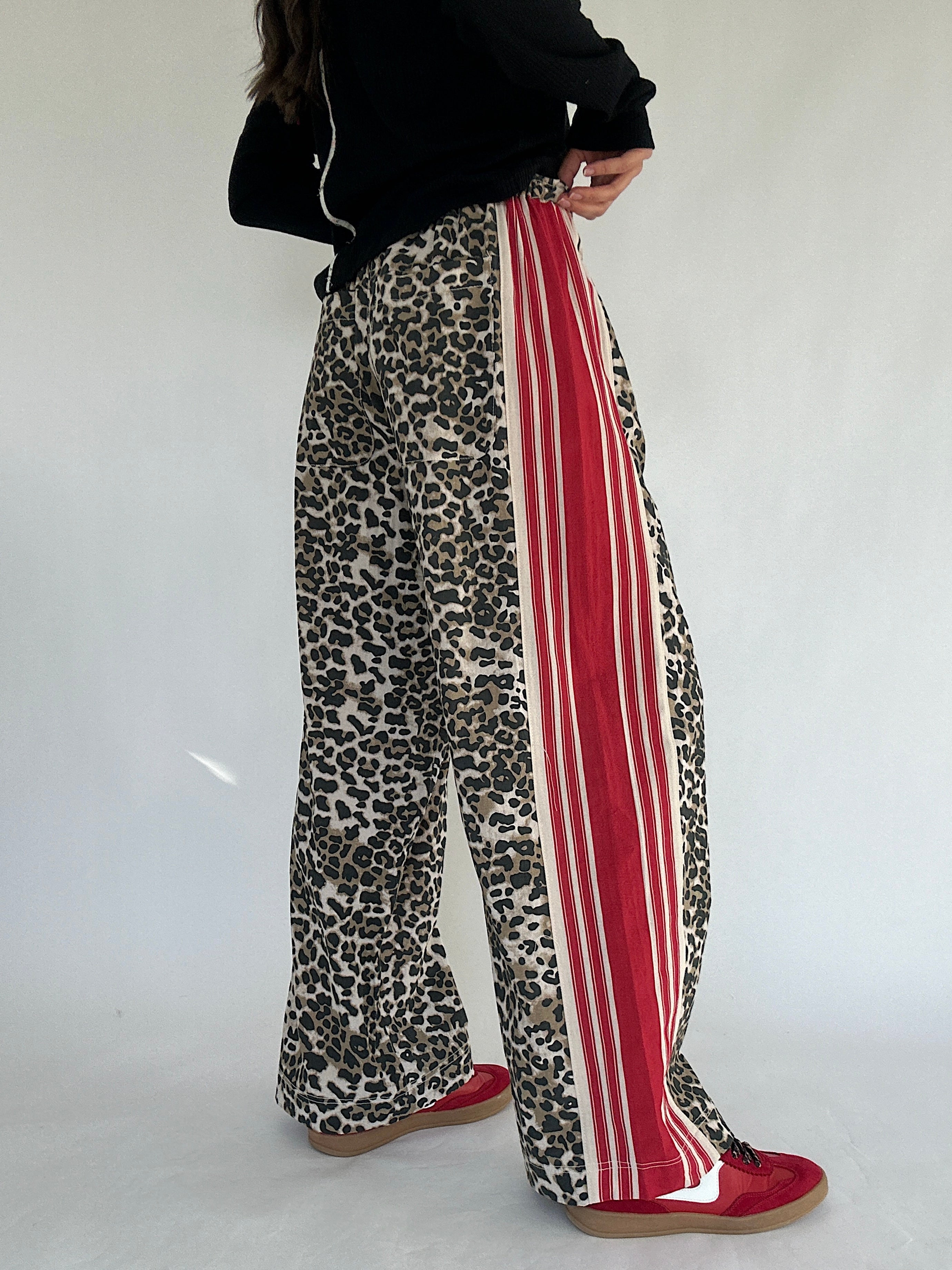 Leopard print pants with red stripes worn by a person on a white background