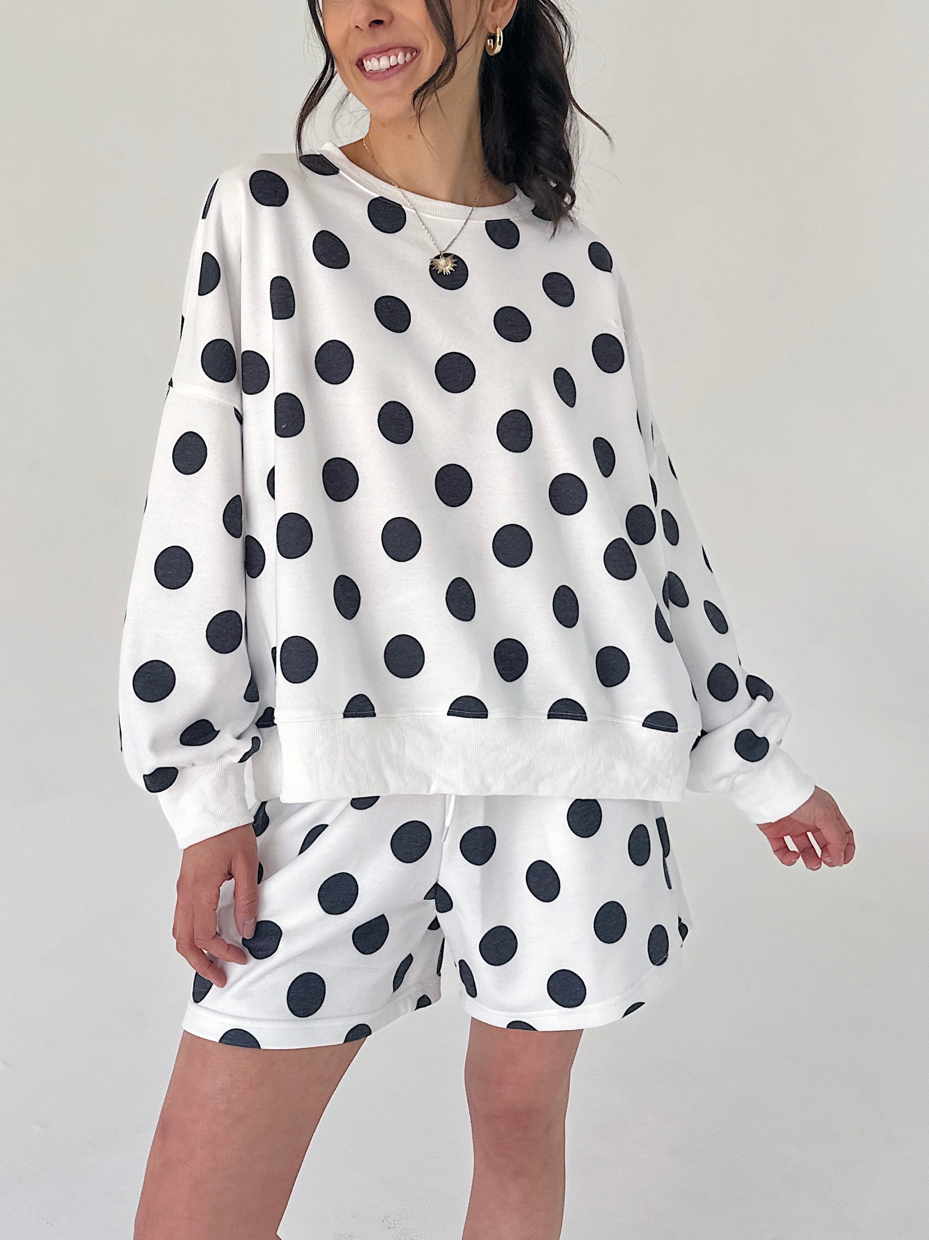 Person wearing a white sweatshirt with black polka dots and matching shorts on a plain background