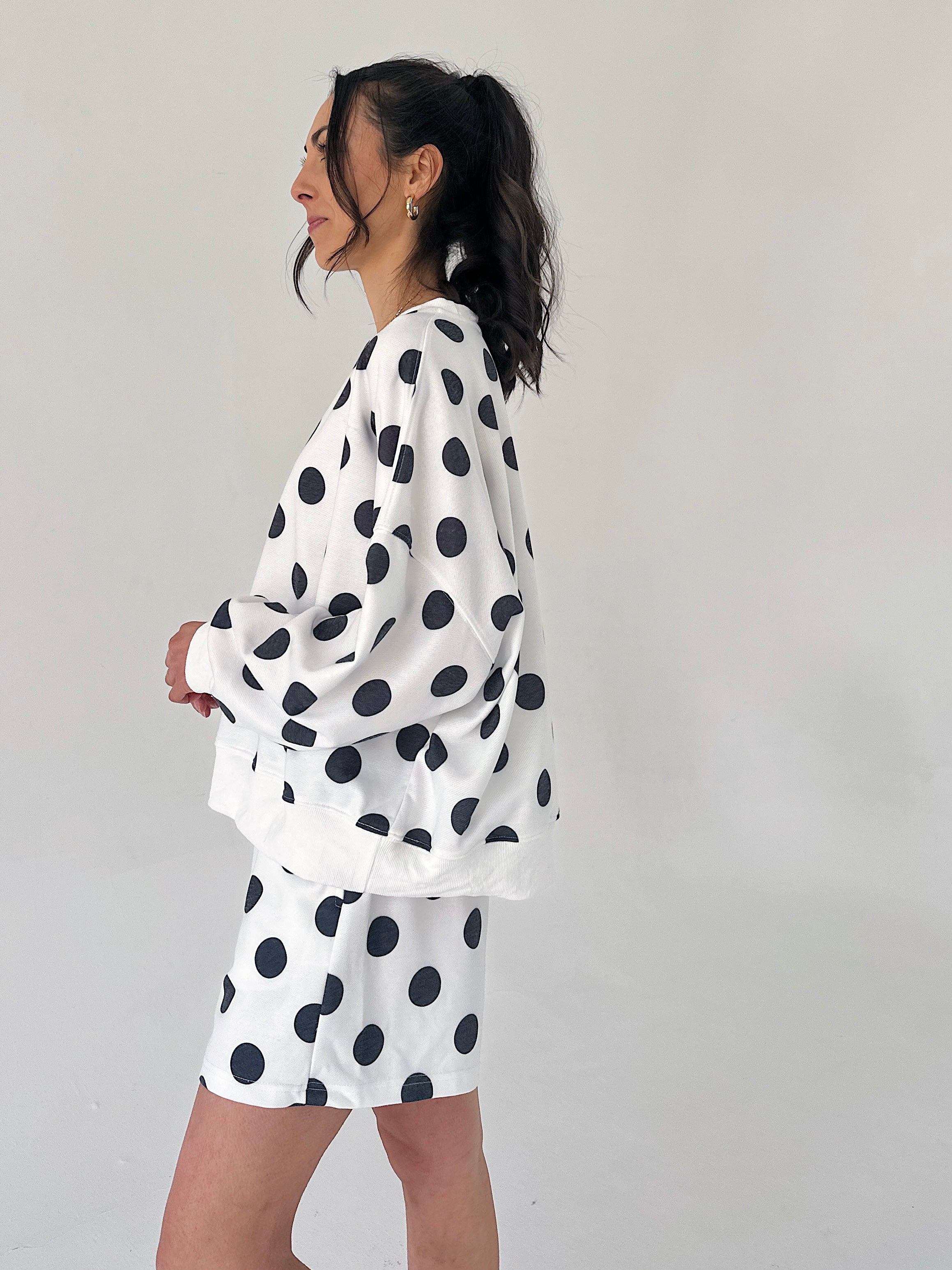 Person wearing a white outfit with black polka dots against a plain background