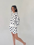 Woman wearing a white outfit with black polka dots on a plain background