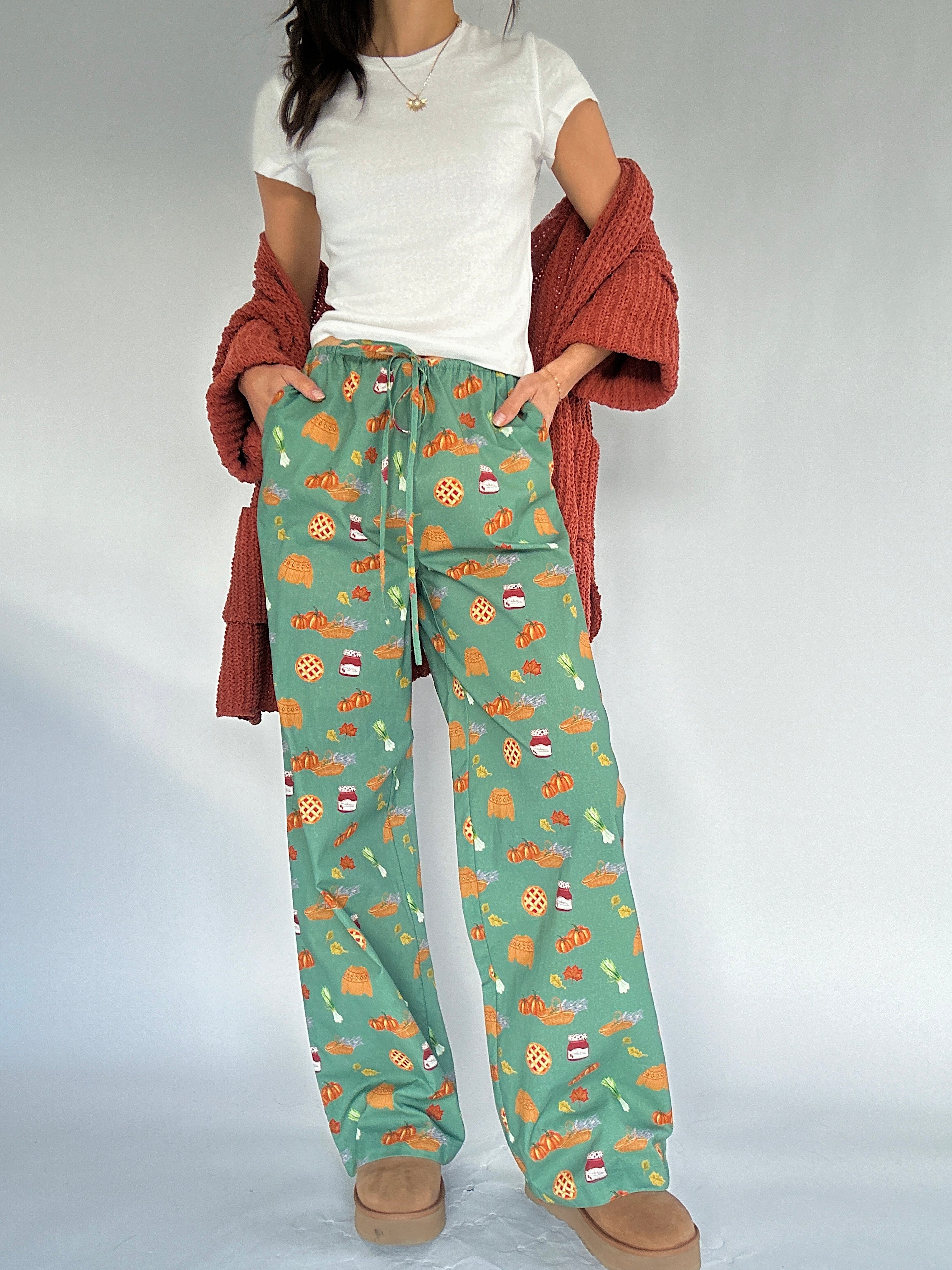 Person wearing green fall patterned pants with a white shirt and rust cardigan sweater on a light gray background