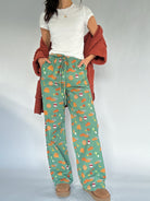 Person wearing green fall patterned pants with a white shirt and rust cardigan sweater on a light gray background