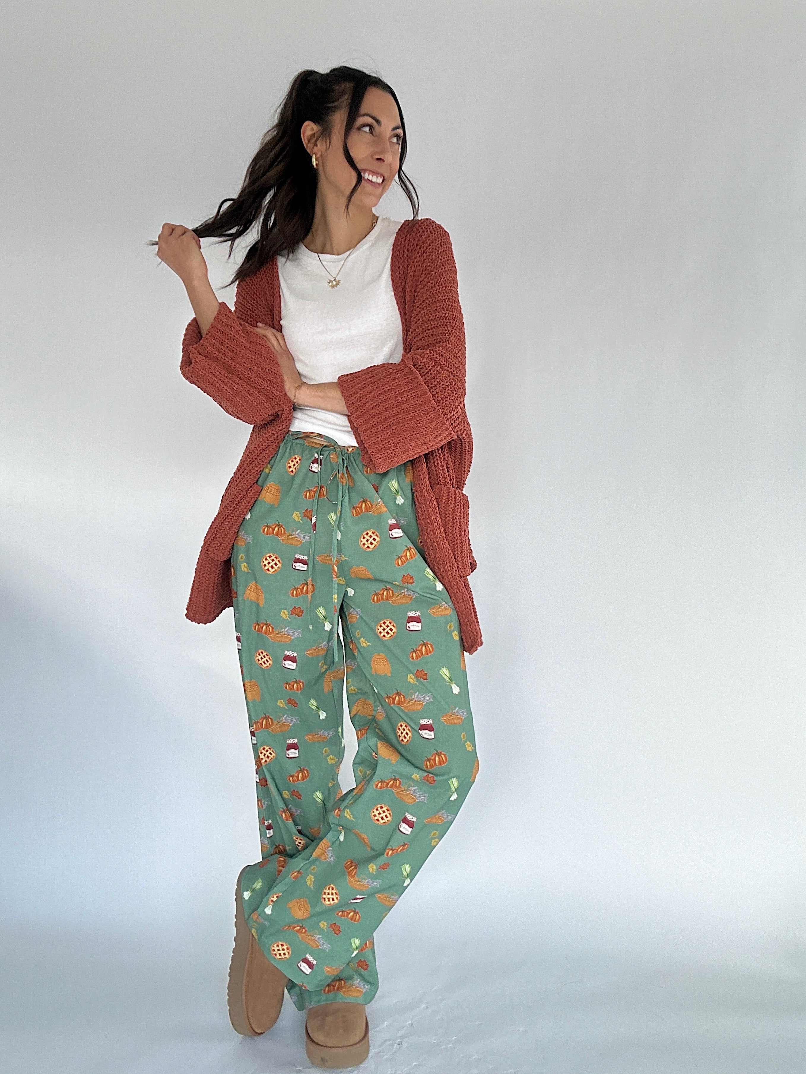 Woman wearing fall patterned green pants and rust cardigan on a white background