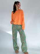 Woman wearing an orange cardigan and green fall inspired patterned pants on a white background