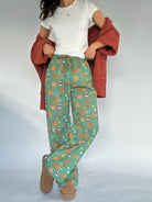 Person wearing green fall patterned pants with a white top and rust cardigan on a plain background