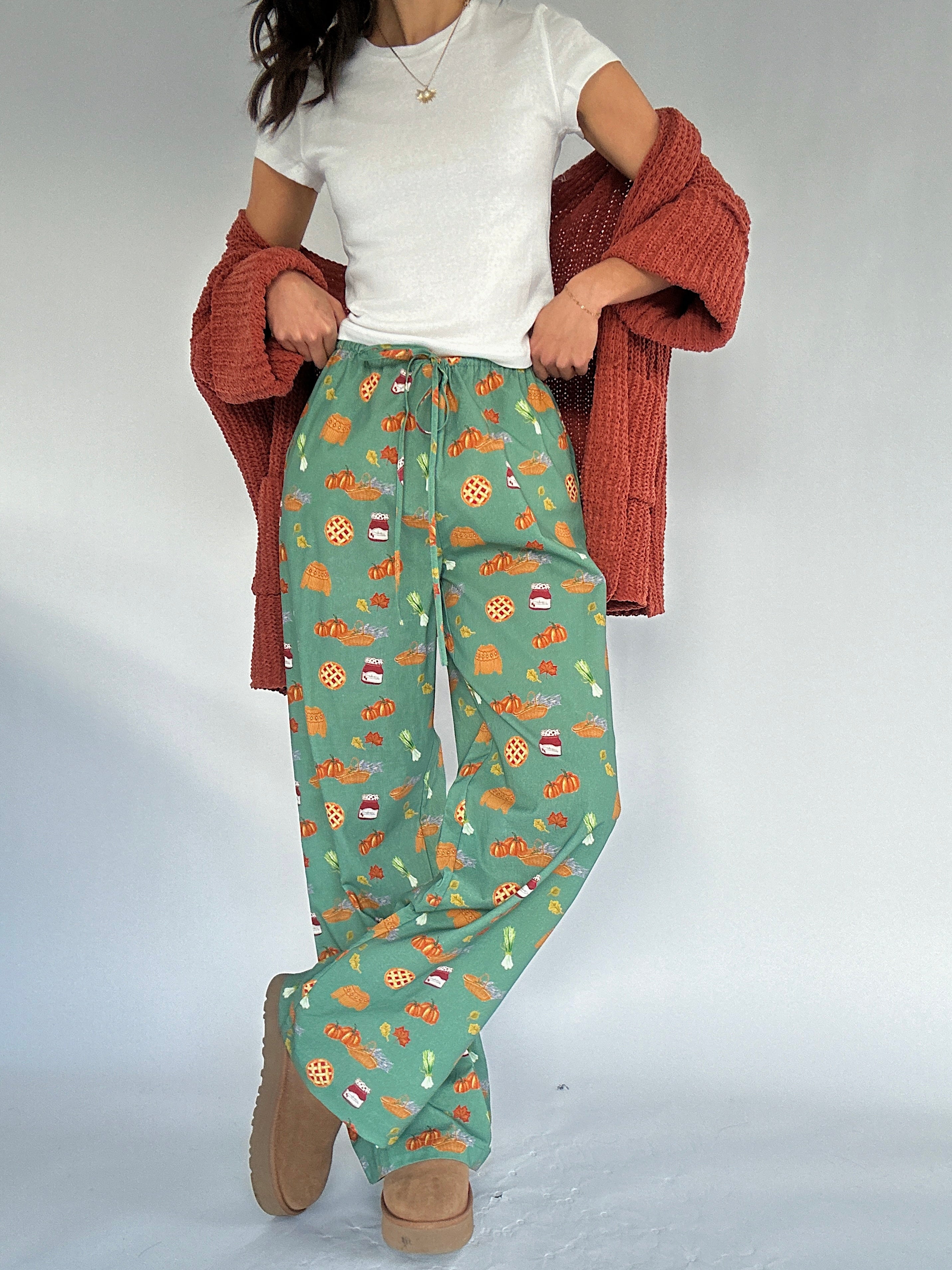 Person wearing green fall patterned pants with a white top and rust cardigan on a plain background