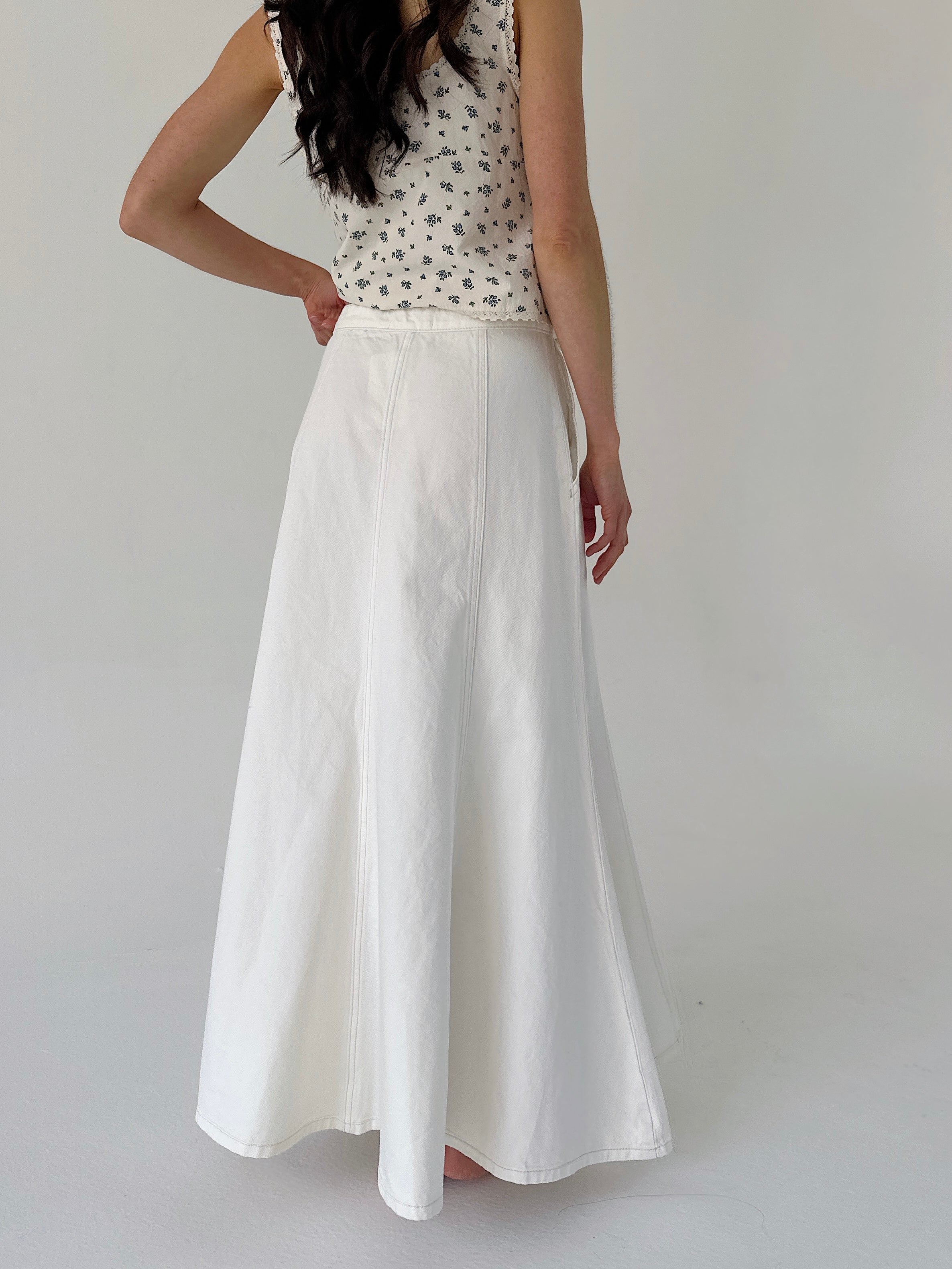 Person wearing a white skirt and patterned top on a plain background