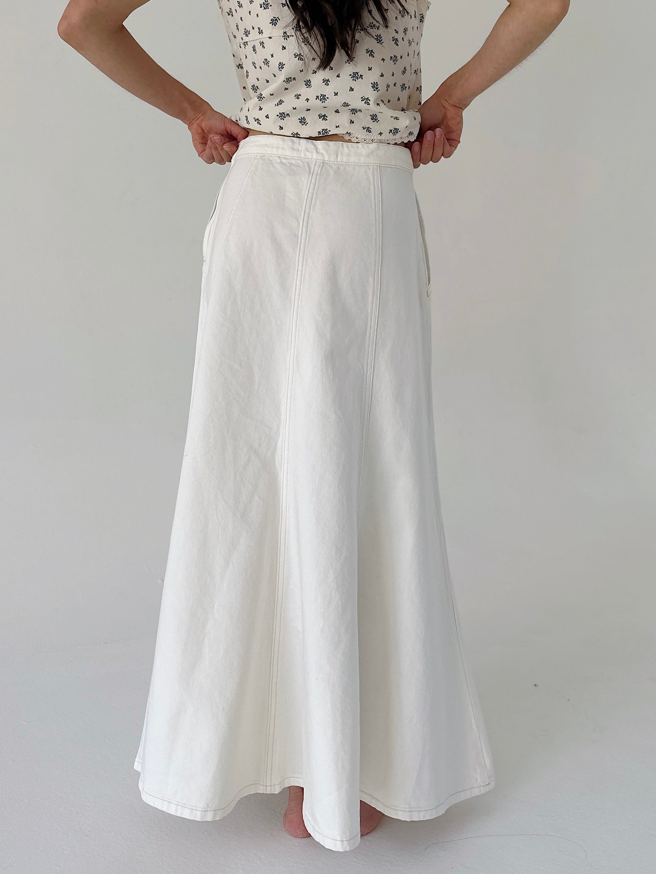 Person wearing a white skirt and patterned top on a plain background