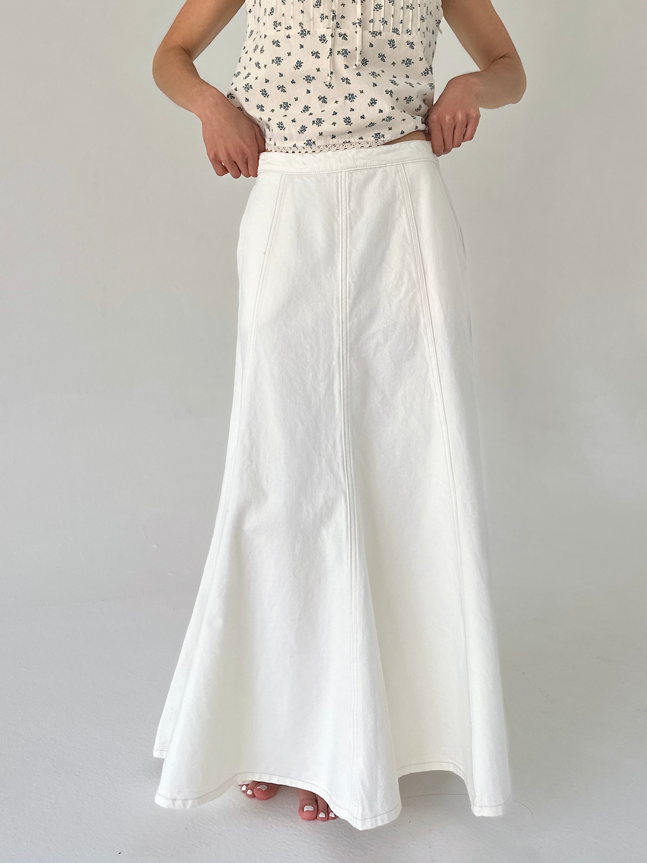 Person wearing a white skirt and patterned top on a plain background