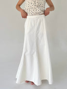 Person wearing a white skirt and patterned top on a plain background