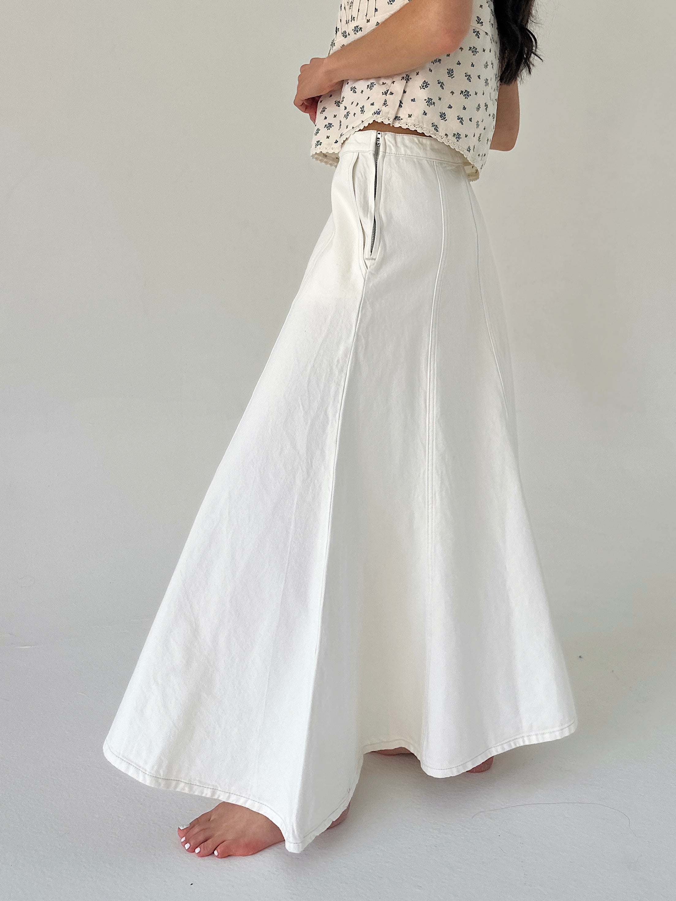 Person wearing white denim maxi skirt on a plain background showing side zipper