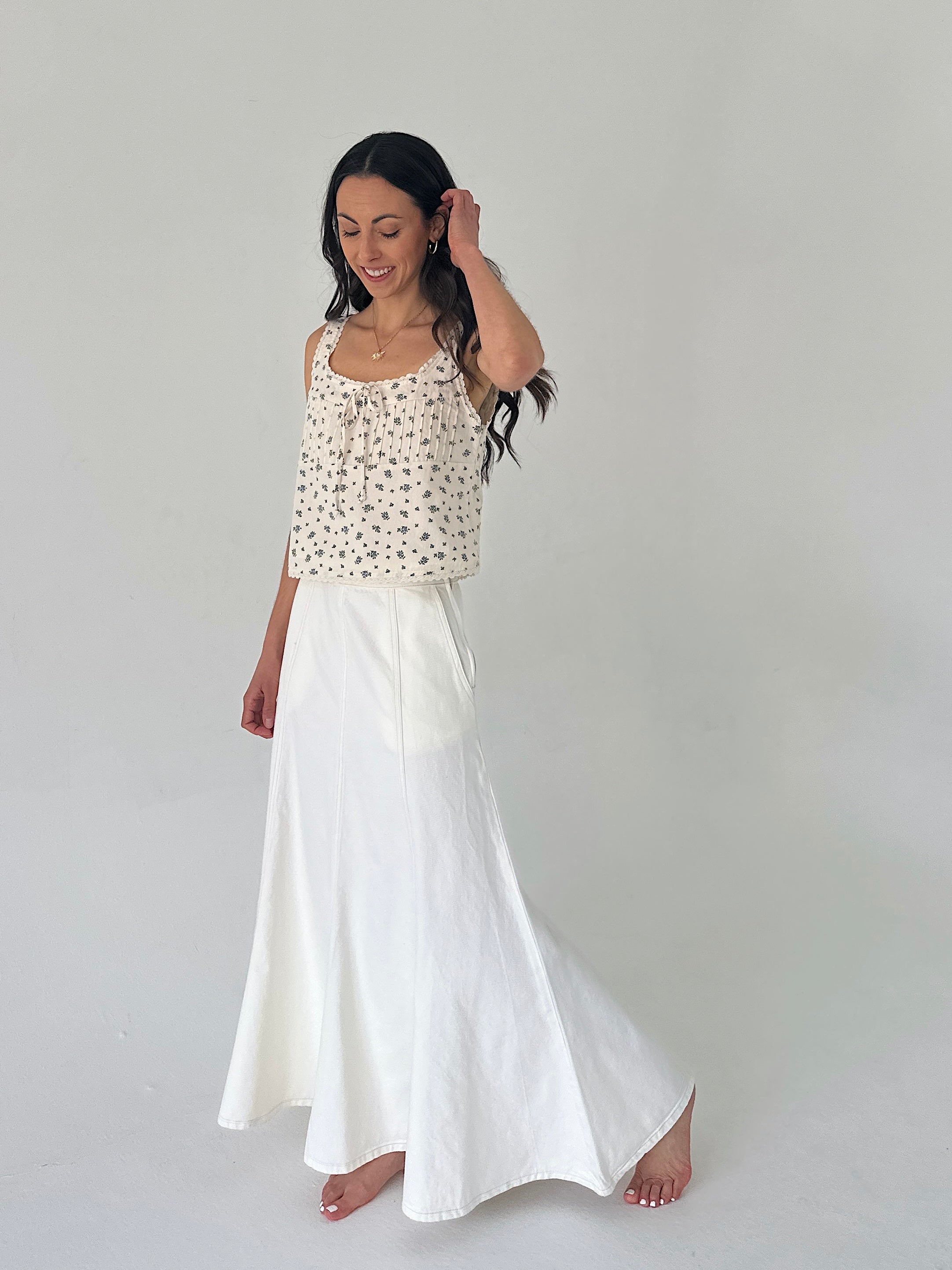 Woman wearing a patterned top and white skirt on a plain background