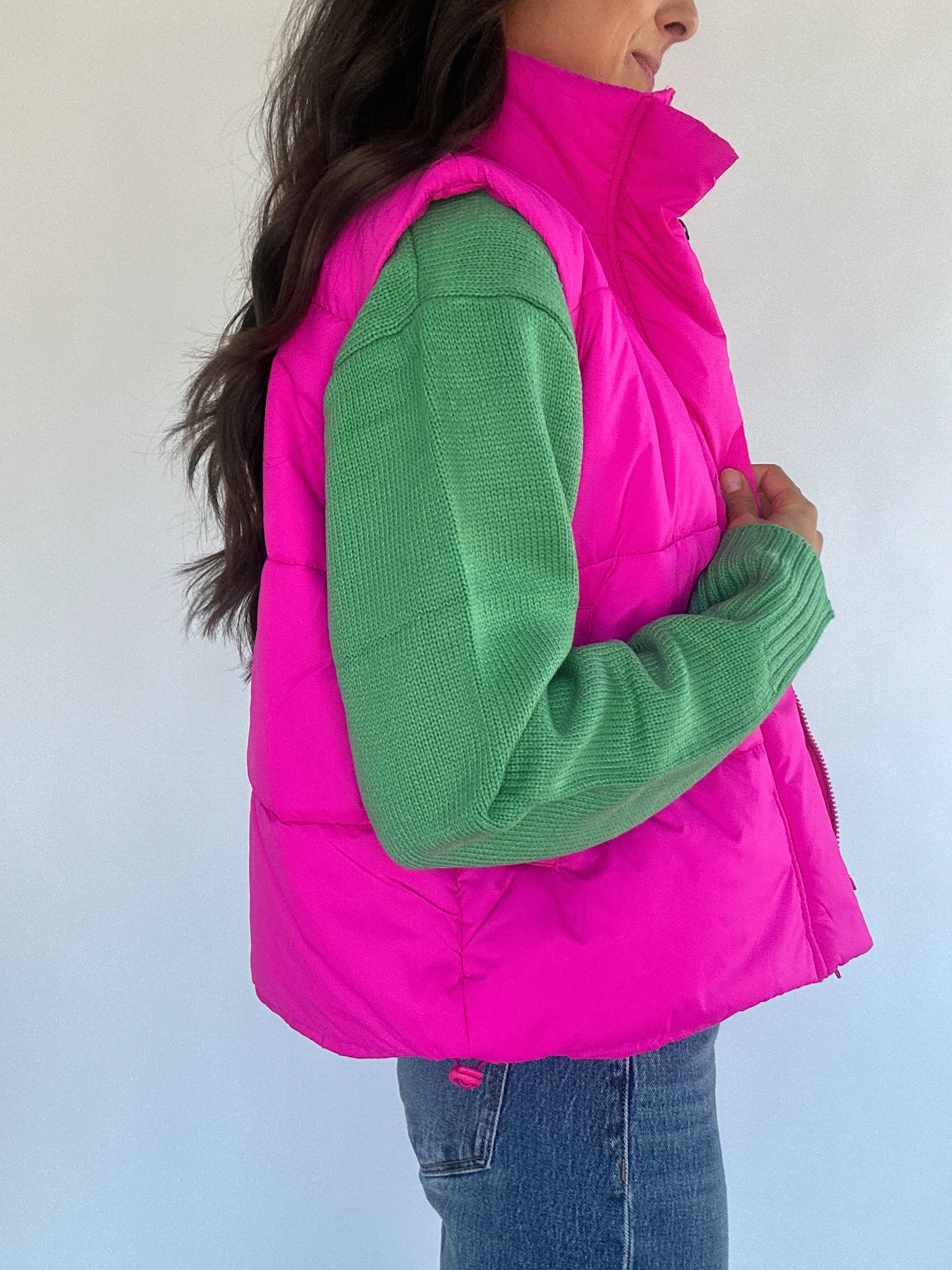 Hot pink puffer vest over a green sweater from side on a plain background