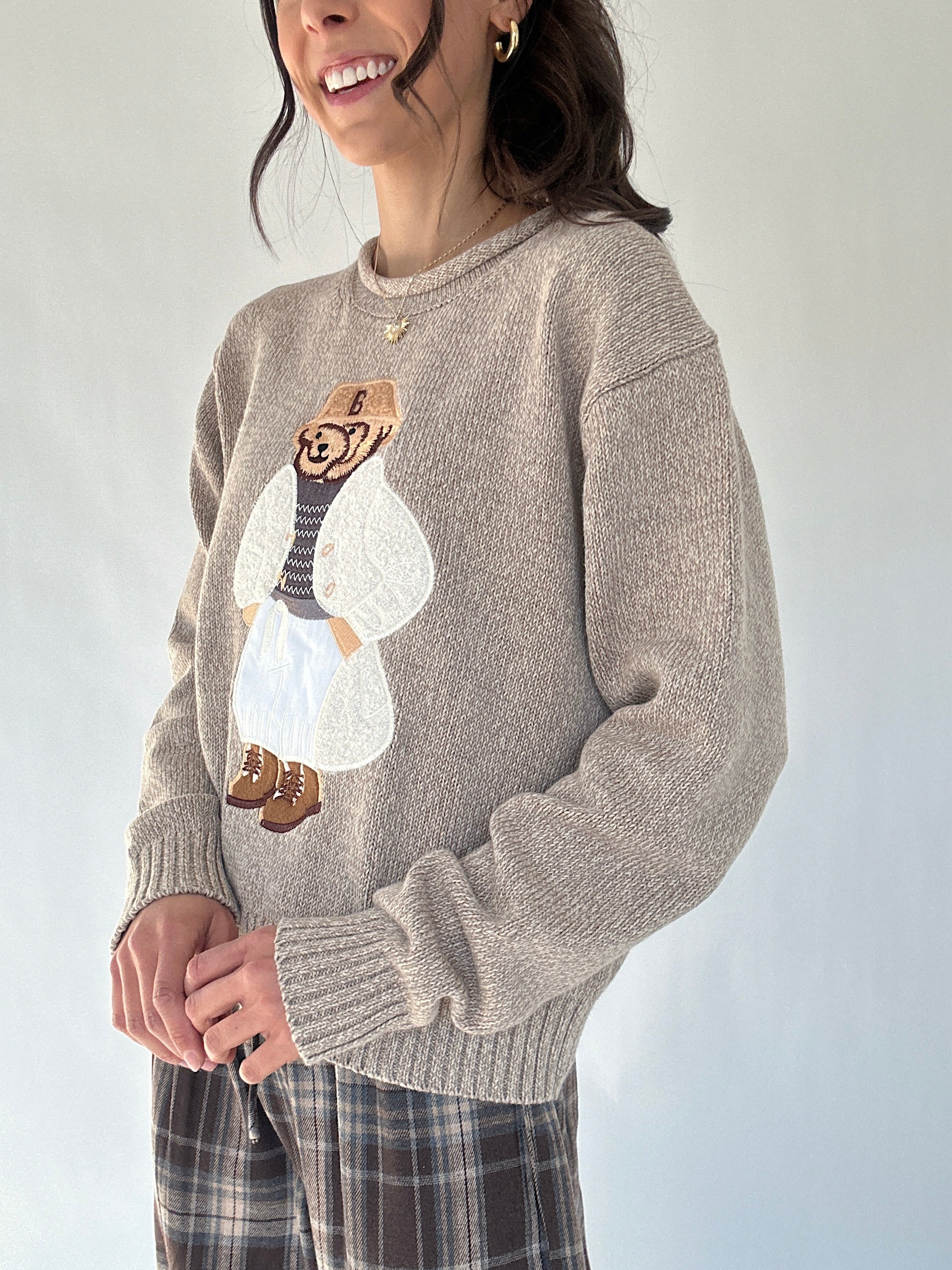 Person wearing a sweater with a teddy bear character design on a plain background from side