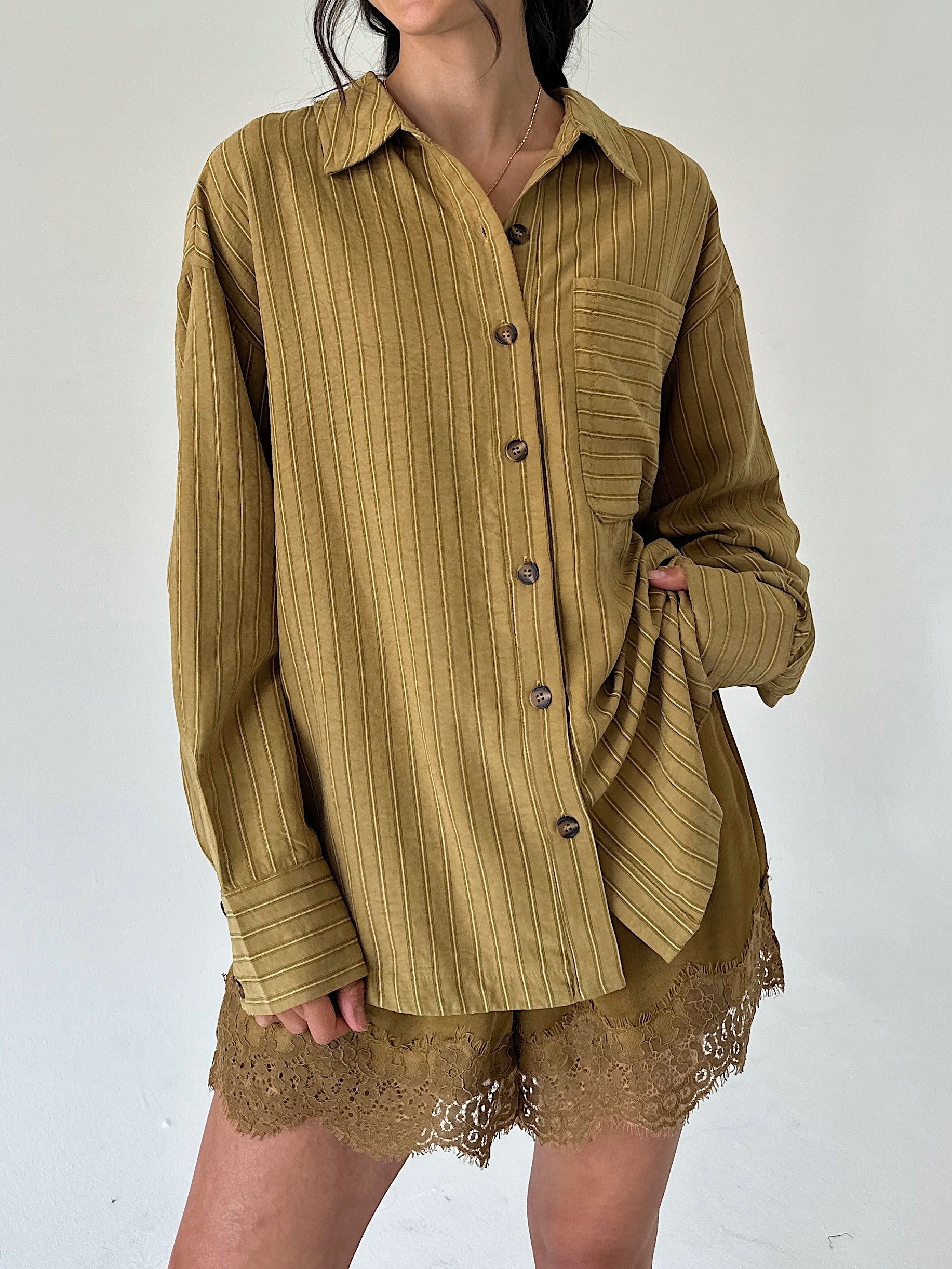 A person wearing an oversized long-sleeve button-front shirt in a warm olive-brown corduroy-like fabric, paired with matching lace-trim shorts, against a plain light background.
