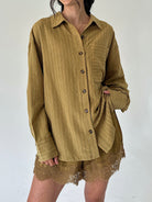 A person wearing an oversized long-sleeve button-front shirt in a warm olive-brown corduroy-like fabric, paired with matching lace-trim shorts, against a plain light background.