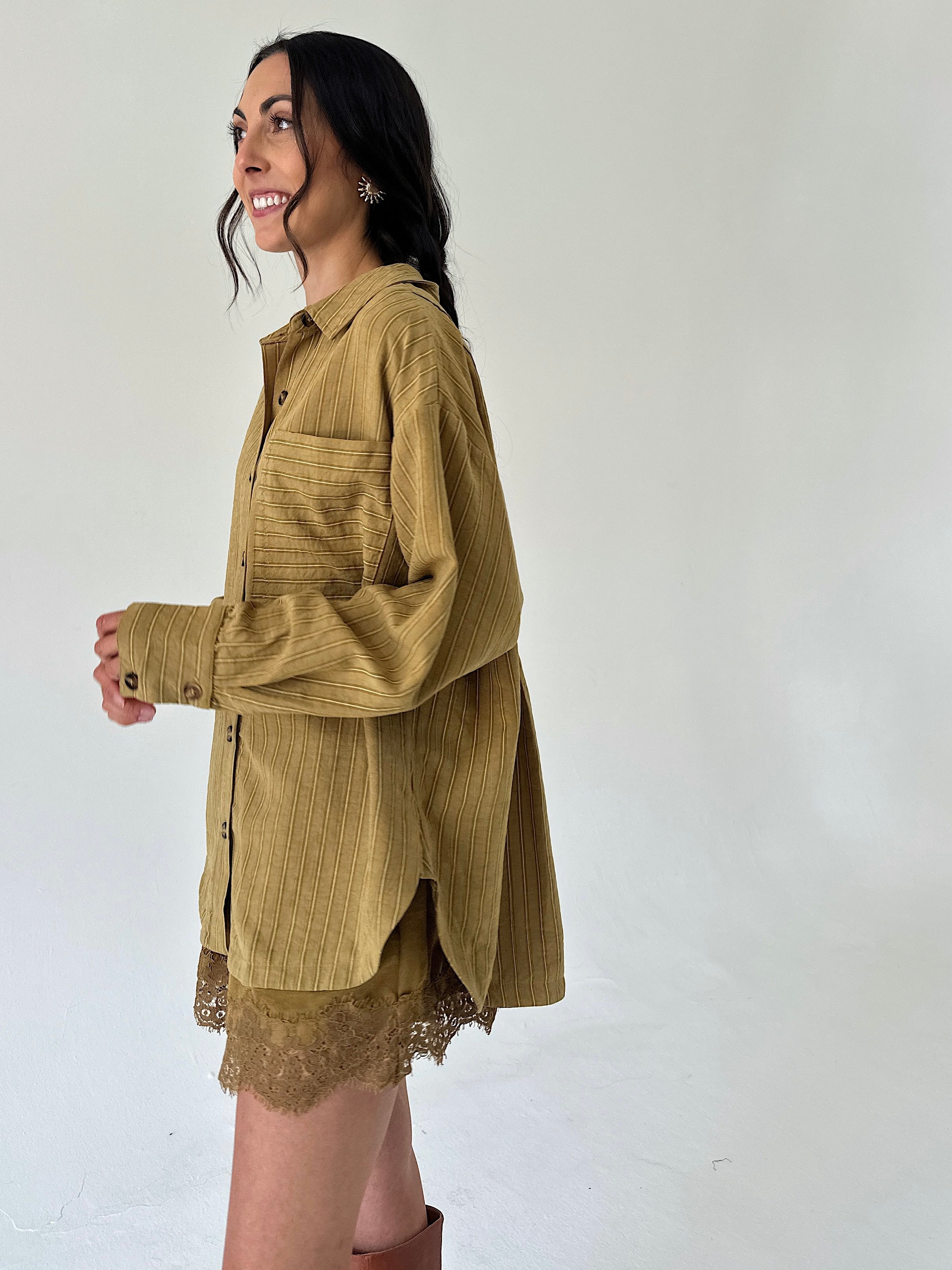 A woman wearing an oversized mustard yellow corduroy button-up shirt with a lace hem, posed against a plain off-white studio background.