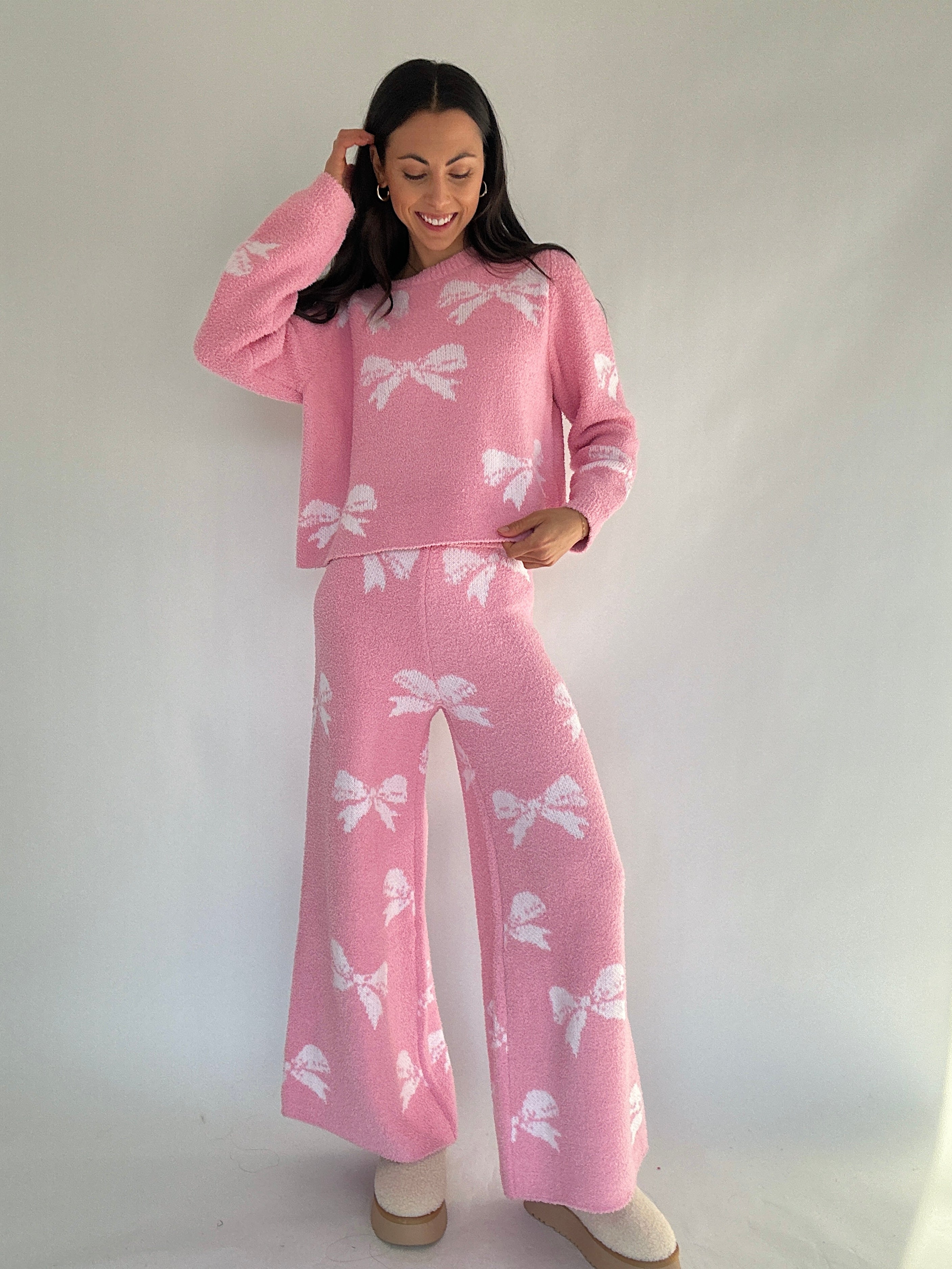 Woman wearing a pink matching lounge outfit with white bow patterns on a plain background