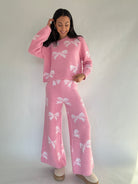 Woman wearing a pink matching lounge outfit with white bow patterns on a plain background