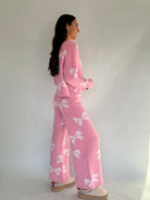 Woman wearing a pink outfit with white bow patterns against a plain background from side