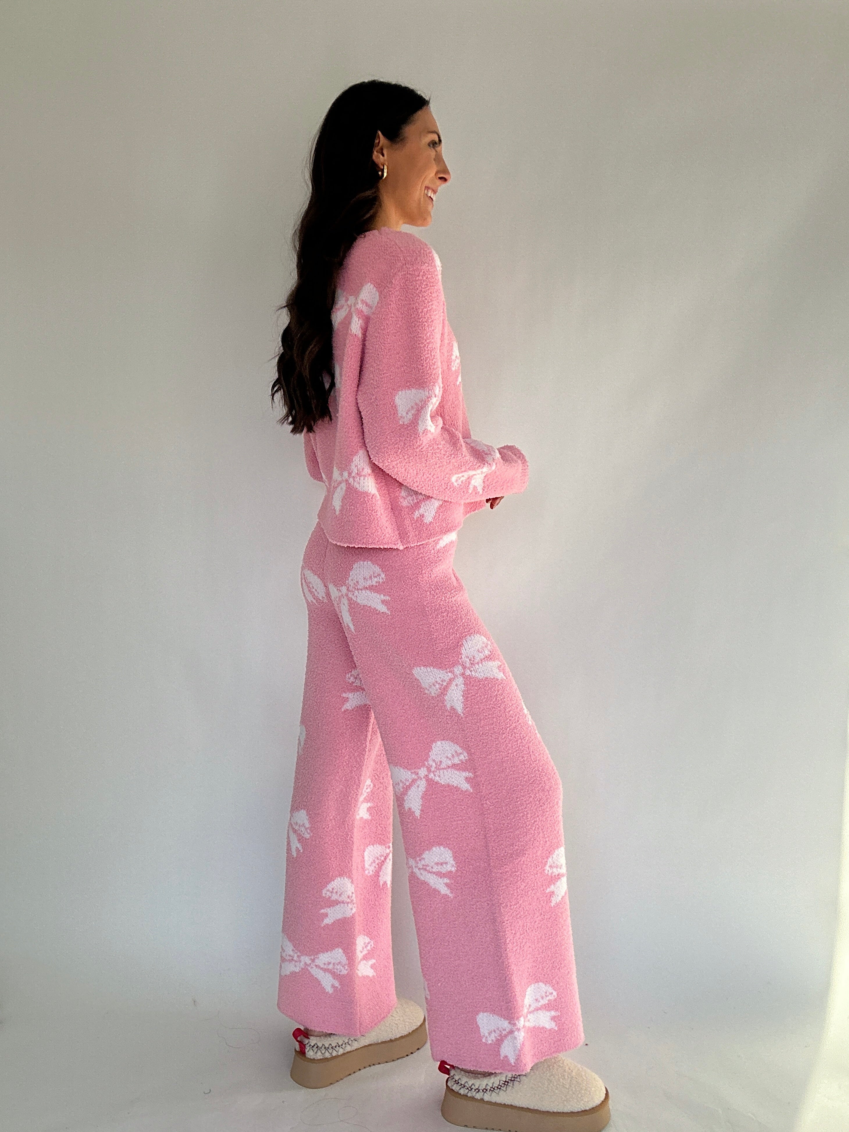 Woman wearing a pink outfit with white bow patterns against a plain background from side