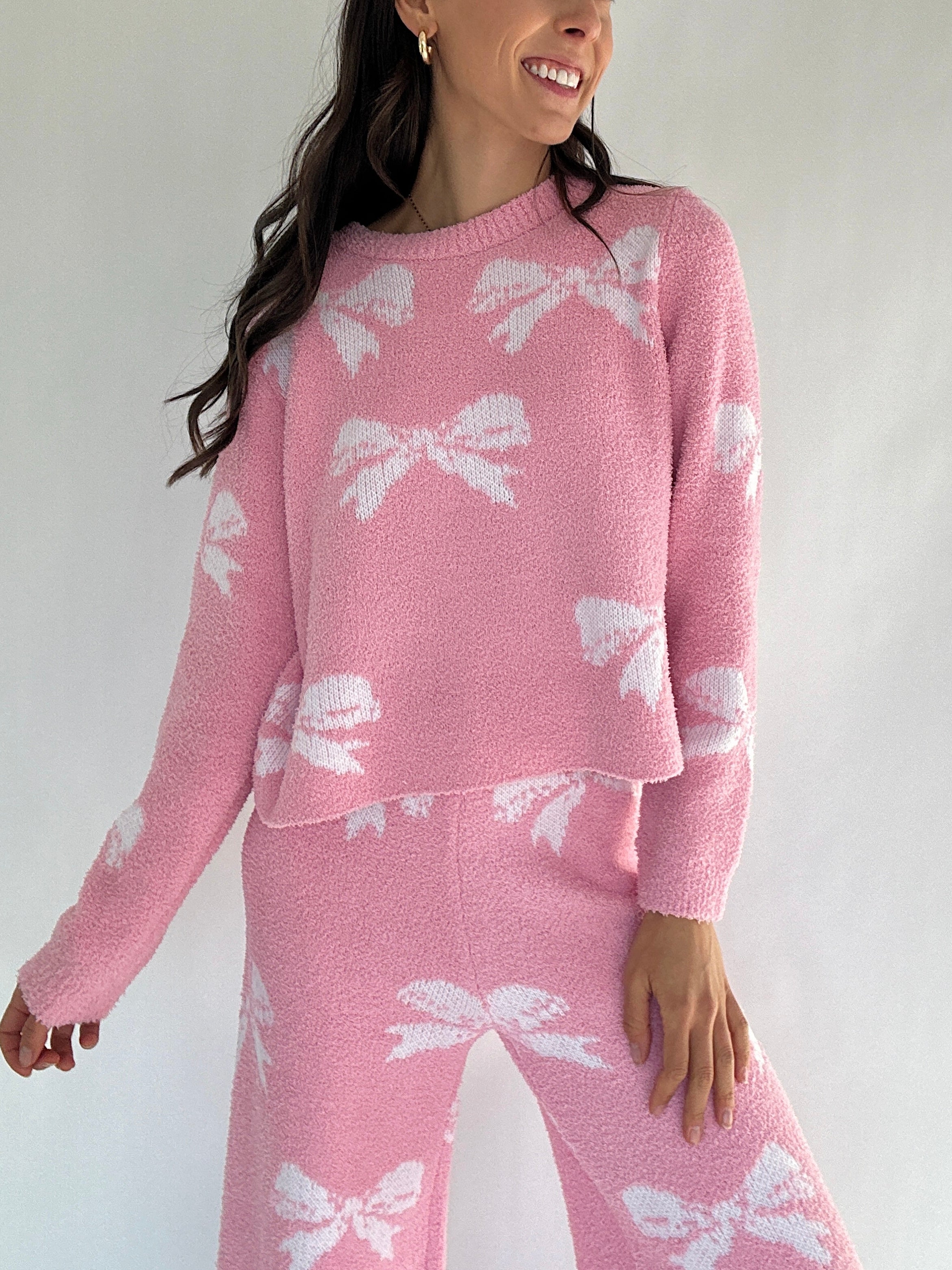 Person wearing a pink sweater with white bow patterns on a plain background with matching pants