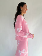 Woman wearing a pink outfit with white bow patterns against a plain background showing top side