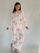 Woman wearing a white matching outfit with pink bows against a plain background