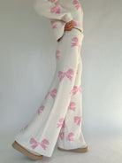 White pants with pink bow patterns worn by a person on a plain background showing side of pants