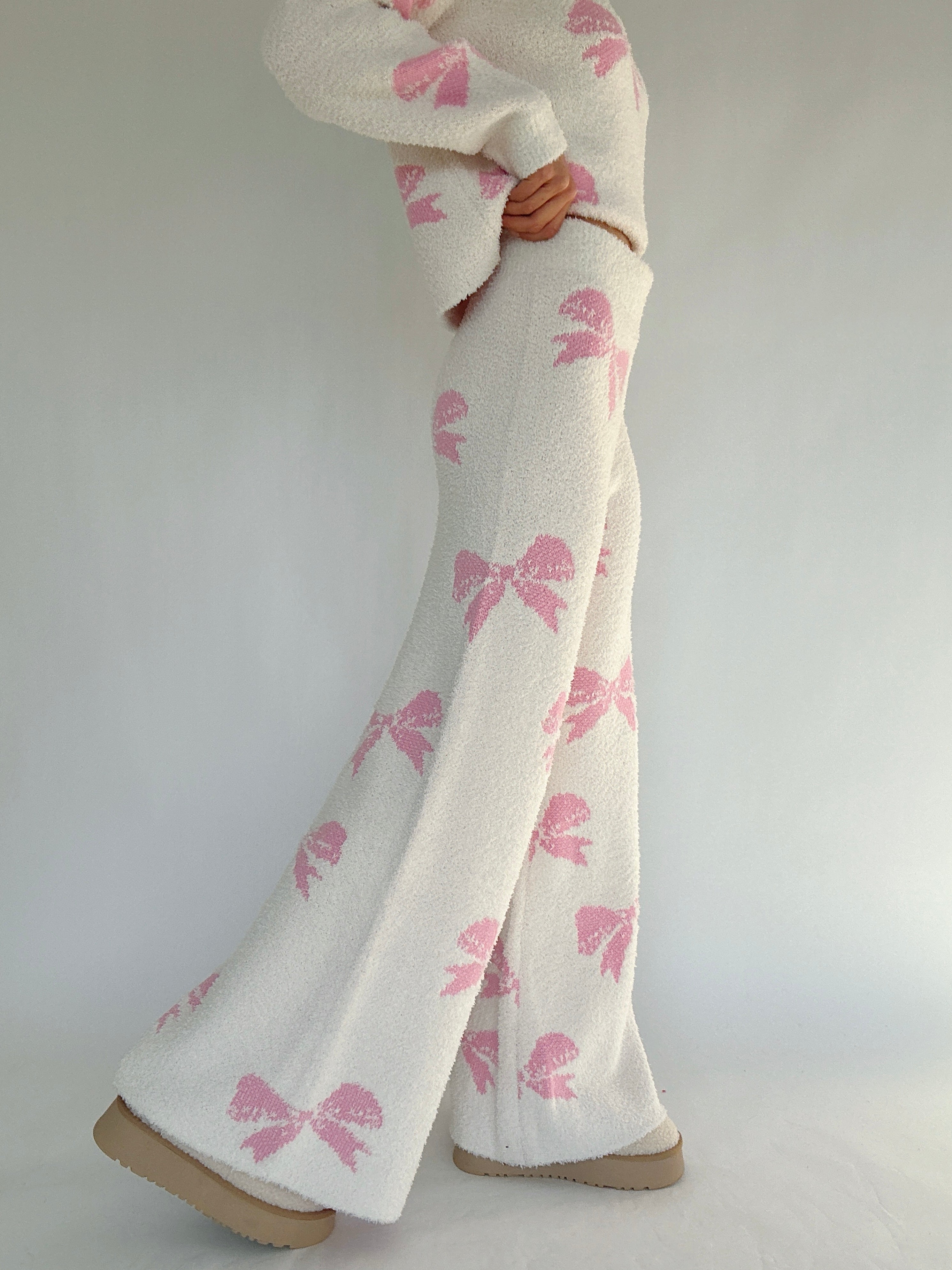 White pants with pink bow patterns worn by a person on a plain background showing side of pants