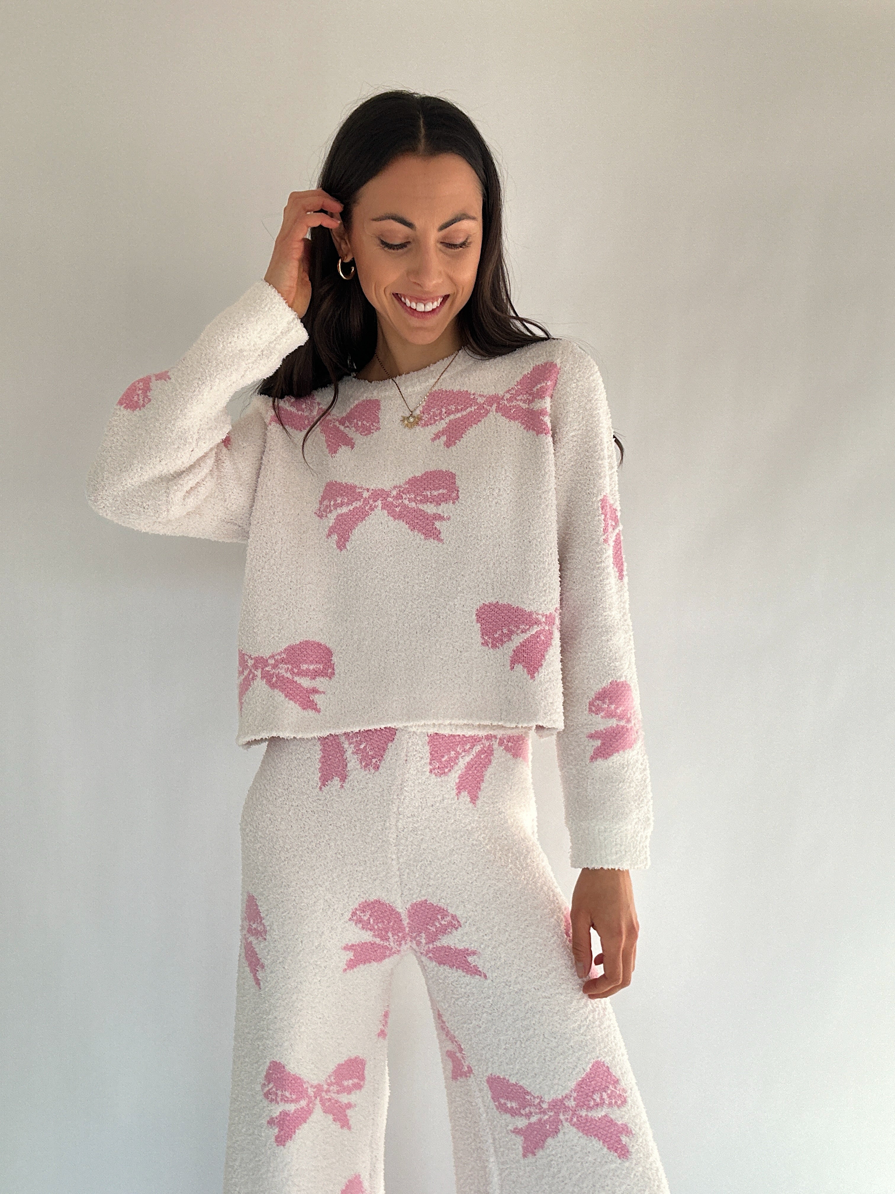 Woman wearing a white sweater and skirt with pink bow patterns against a plain background