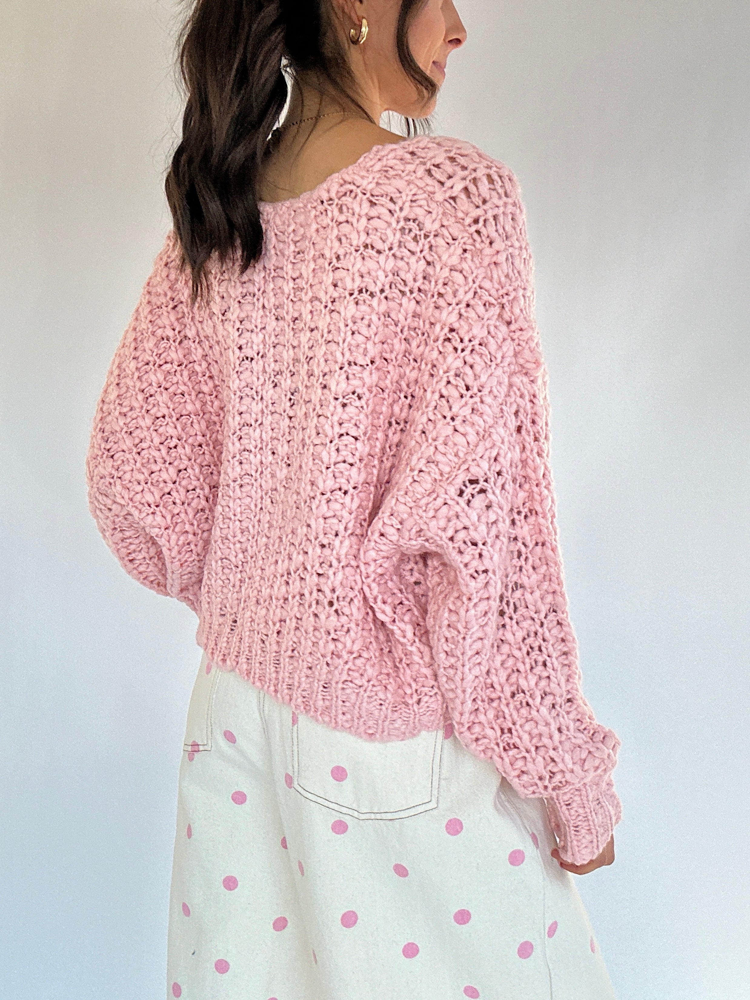 Person wearing a pink knitted sweater and white pants with pink polka dots against a plain background back view