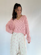 Woman wearing a pink knitted sweater and white pants with pink polka dots against a plain background