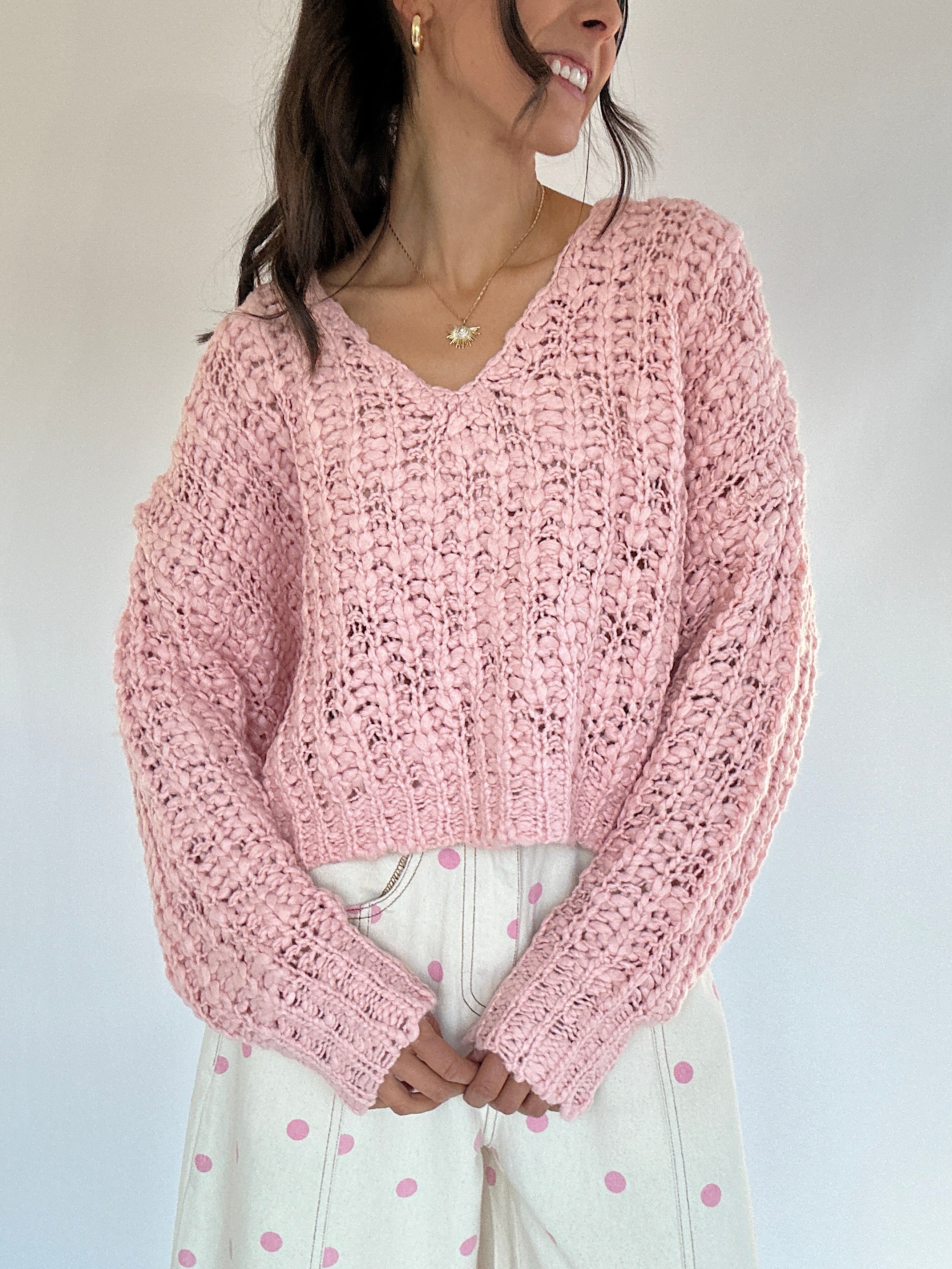 Person wearing a pink knitted sweater against a plain background