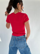 Person wearing a red t-shirt and blue jeans against a white background back view