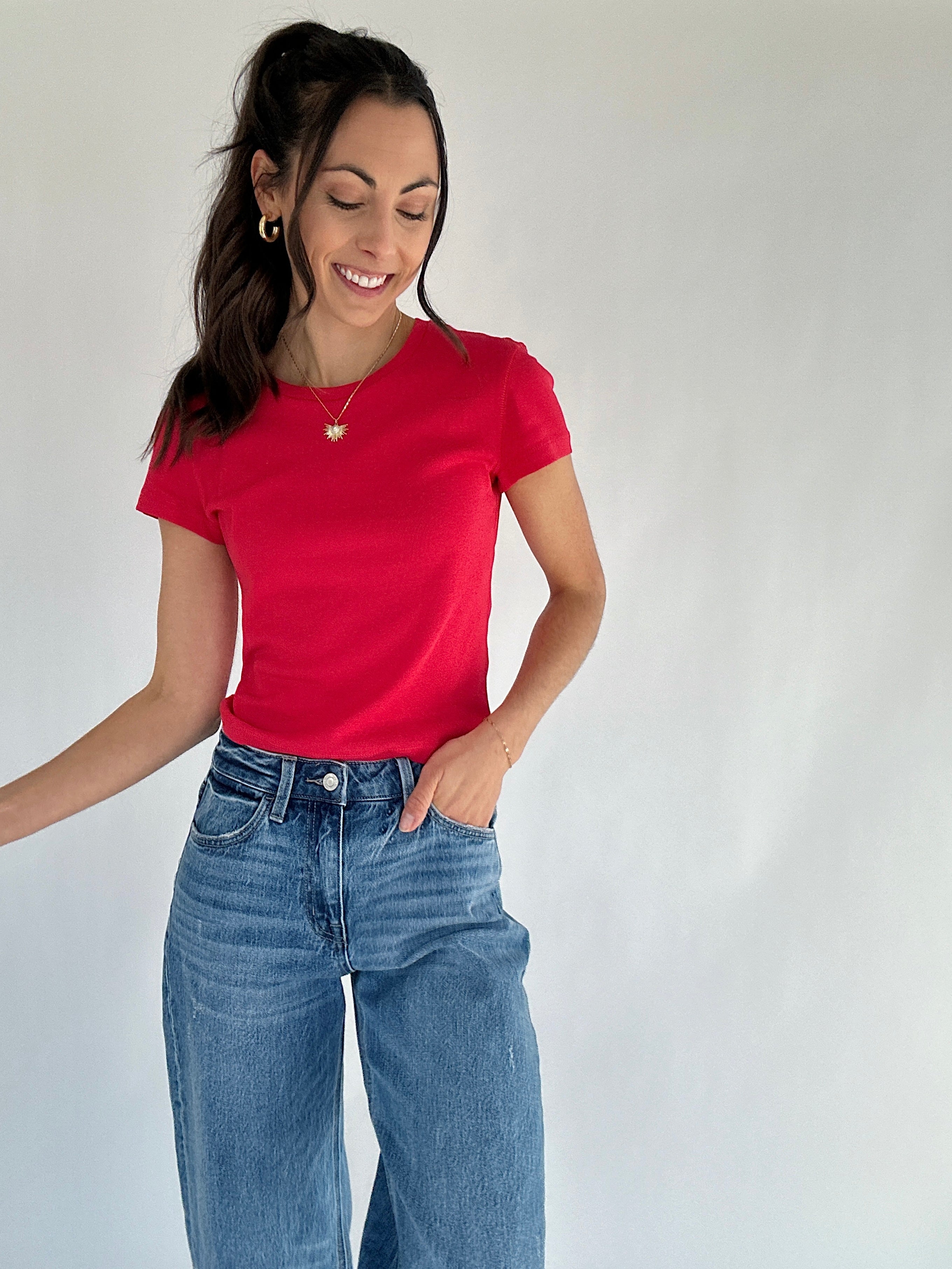 Woman wearing a red t-shirt and blue jeans against a plain background